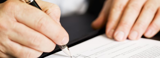Businessman sitting at office desk signing a contract with shallow focus on signature.