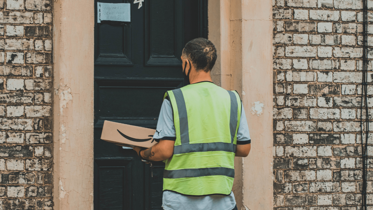 Entregador da Amazon segurando pacote na porta de cliente (Imagem: Super Straho/Unsplash)