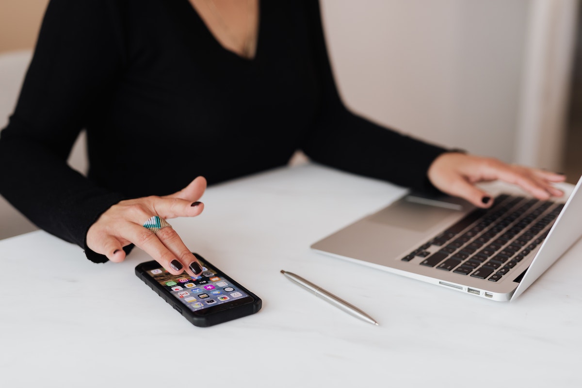 Uma mulher com uma mão no celular e outra mão no computador