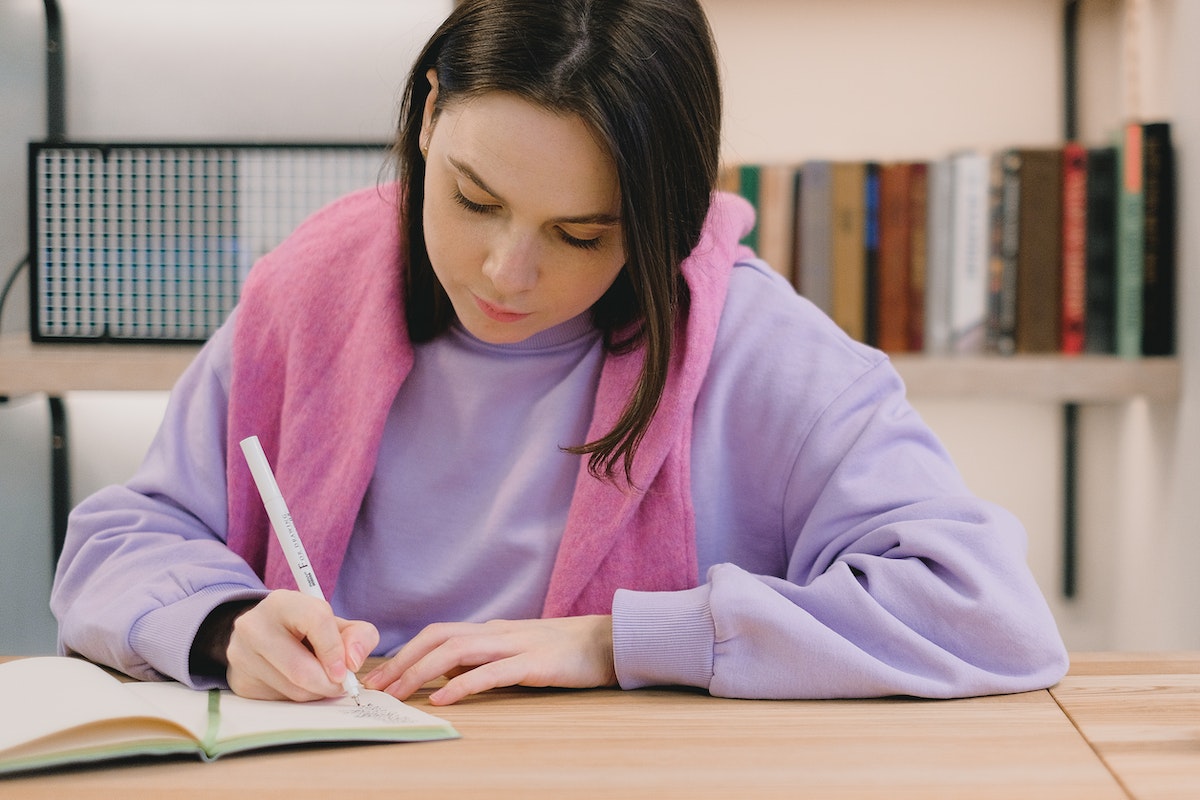 Uma mulher vestida com um moletom rosa escrevendo em um caderno inteligente