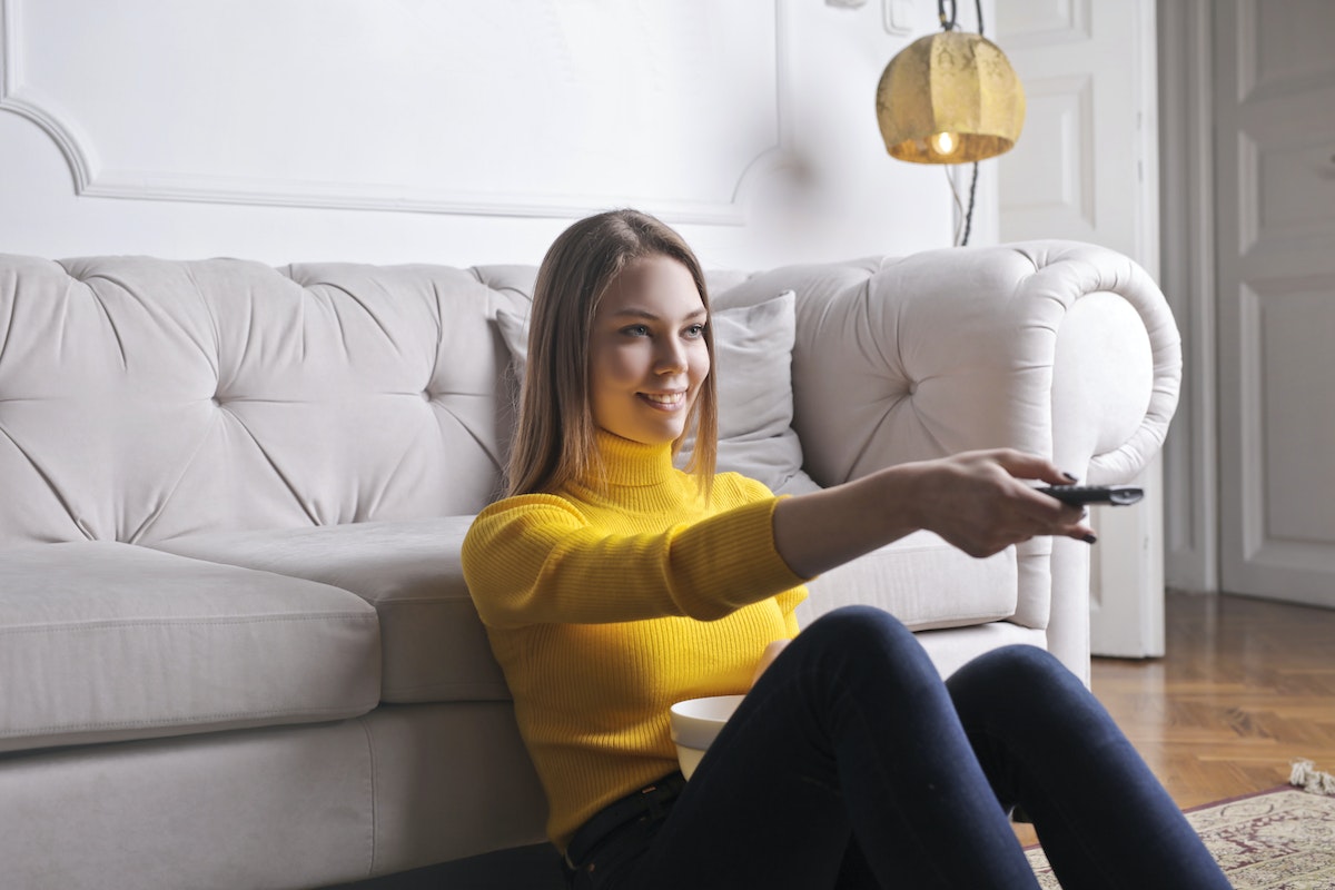 Mulher sentada em frente ao sofá enquanto aponta o controle em direção à Televisão 