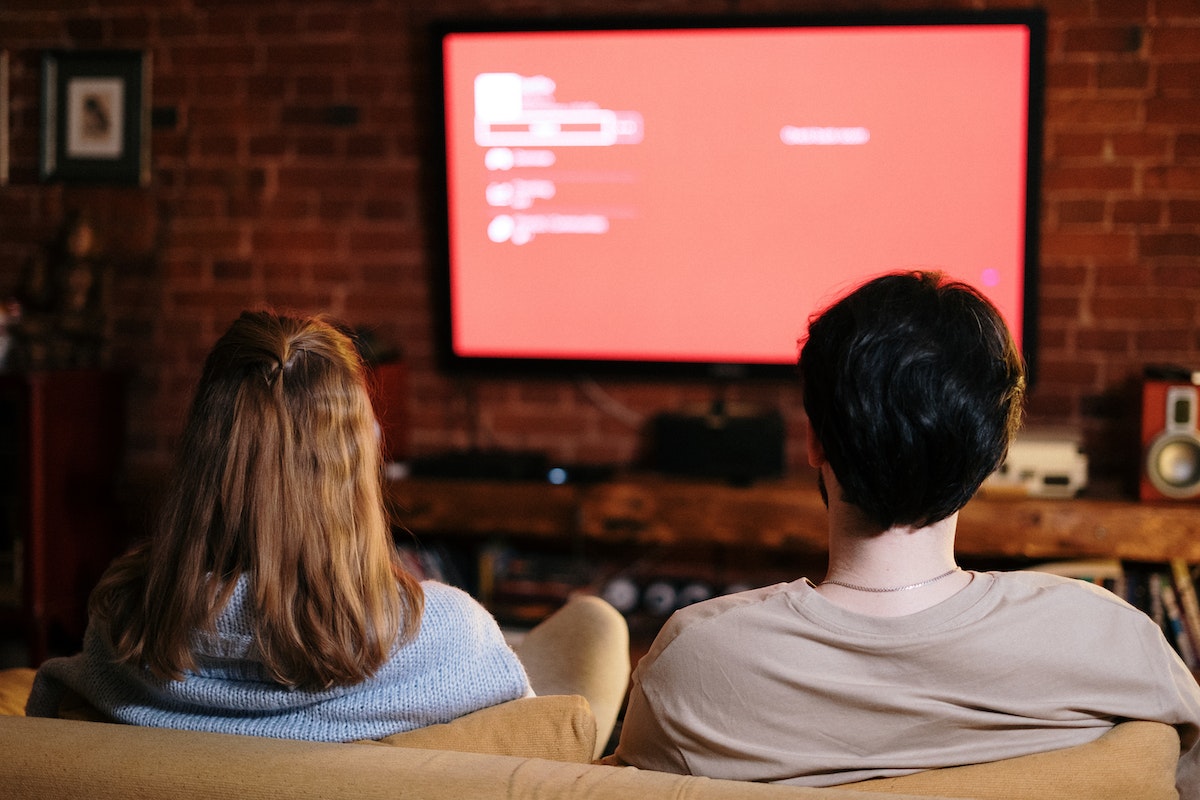 Duas pessoas estão vendo televisão. A tela está vermelha