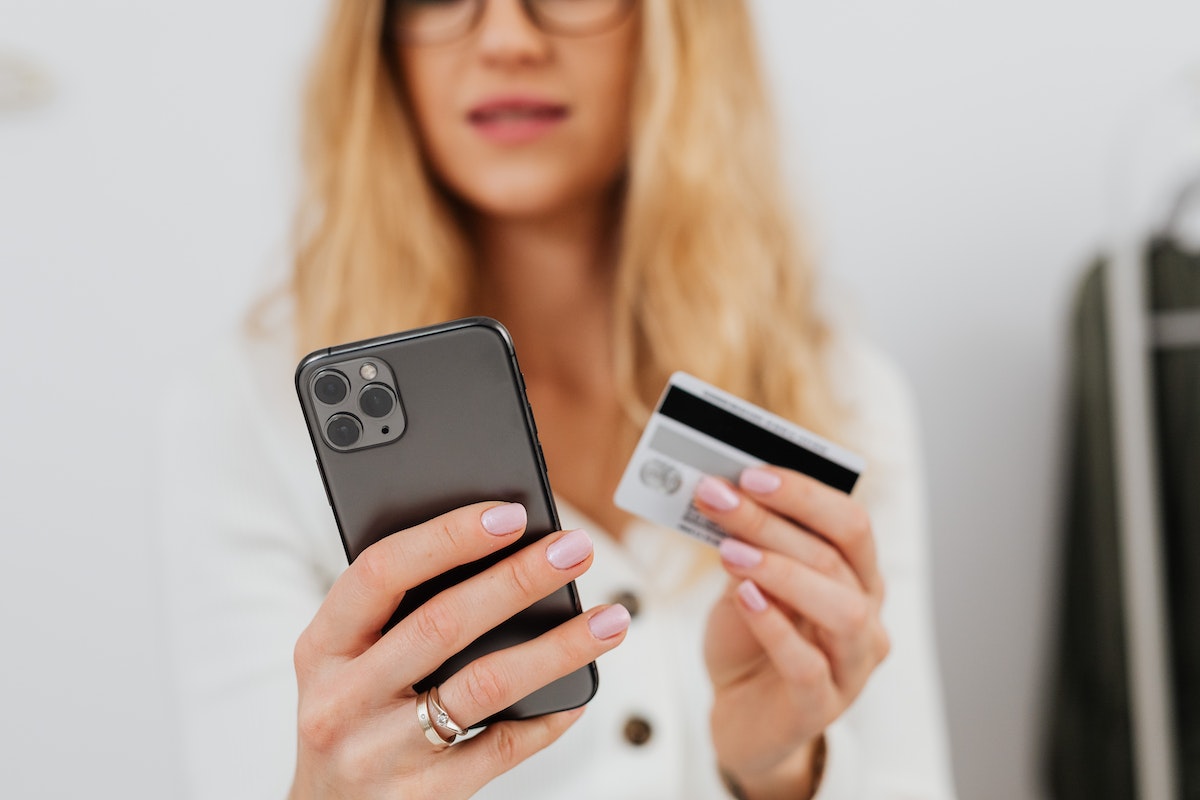 Uma mulher com um iPhone em uma mão, e o cartão de crédito na outra