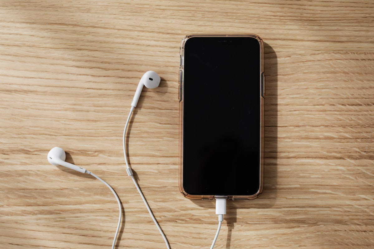 Celular em cima de uma mesa de madeira com o fone de ouvido conectado