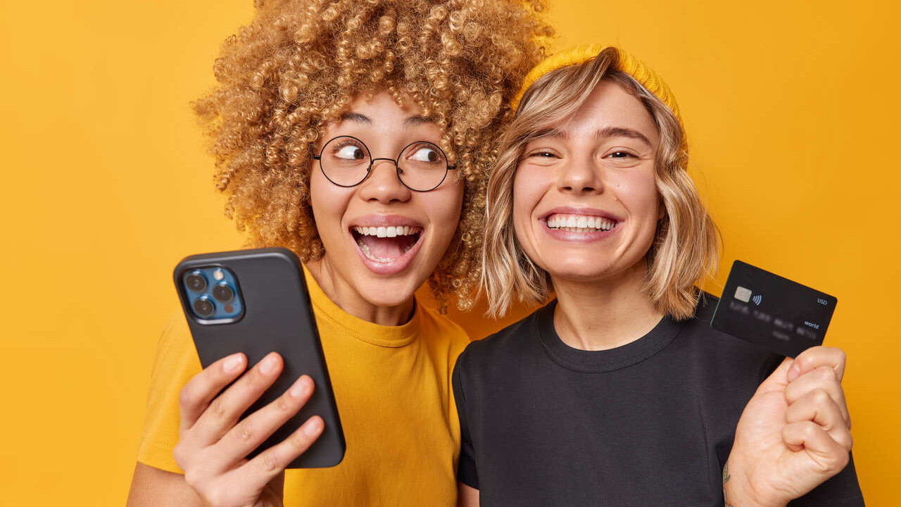 Garotas fazendo compras pelo celular com cartão de crédito na mão durante a Black Friday