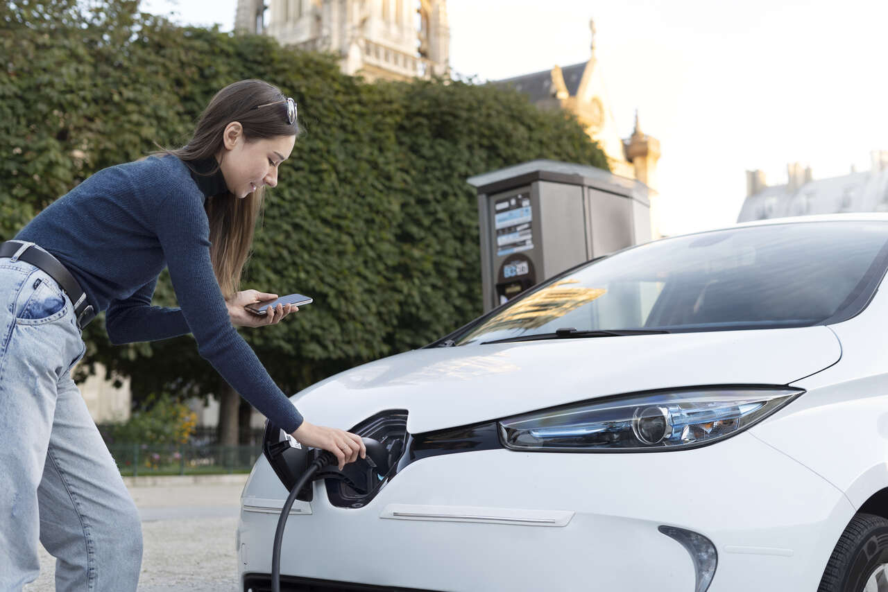 Mulher recarregando carro elétrico com celular na mão