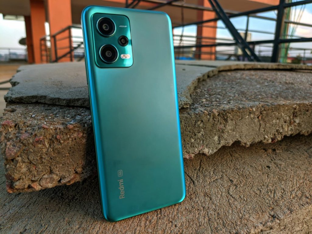 Xiaomi Redmi Note 12 5G na cor verde, encostado em um bloco de cimento