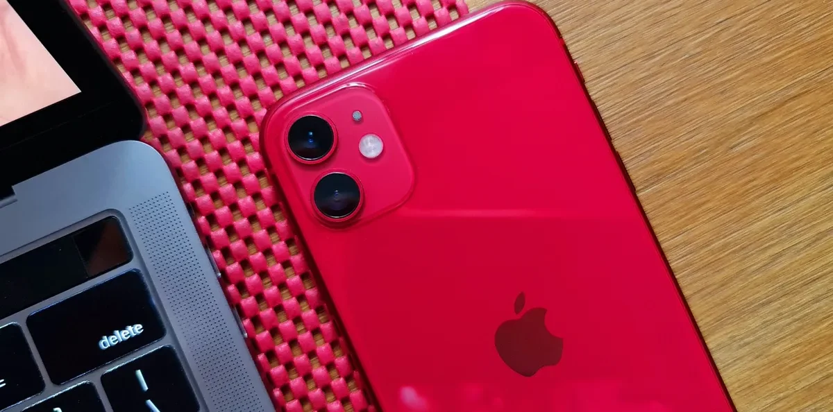 Celular iPhone na cor vermelha, ao lado de um notebook