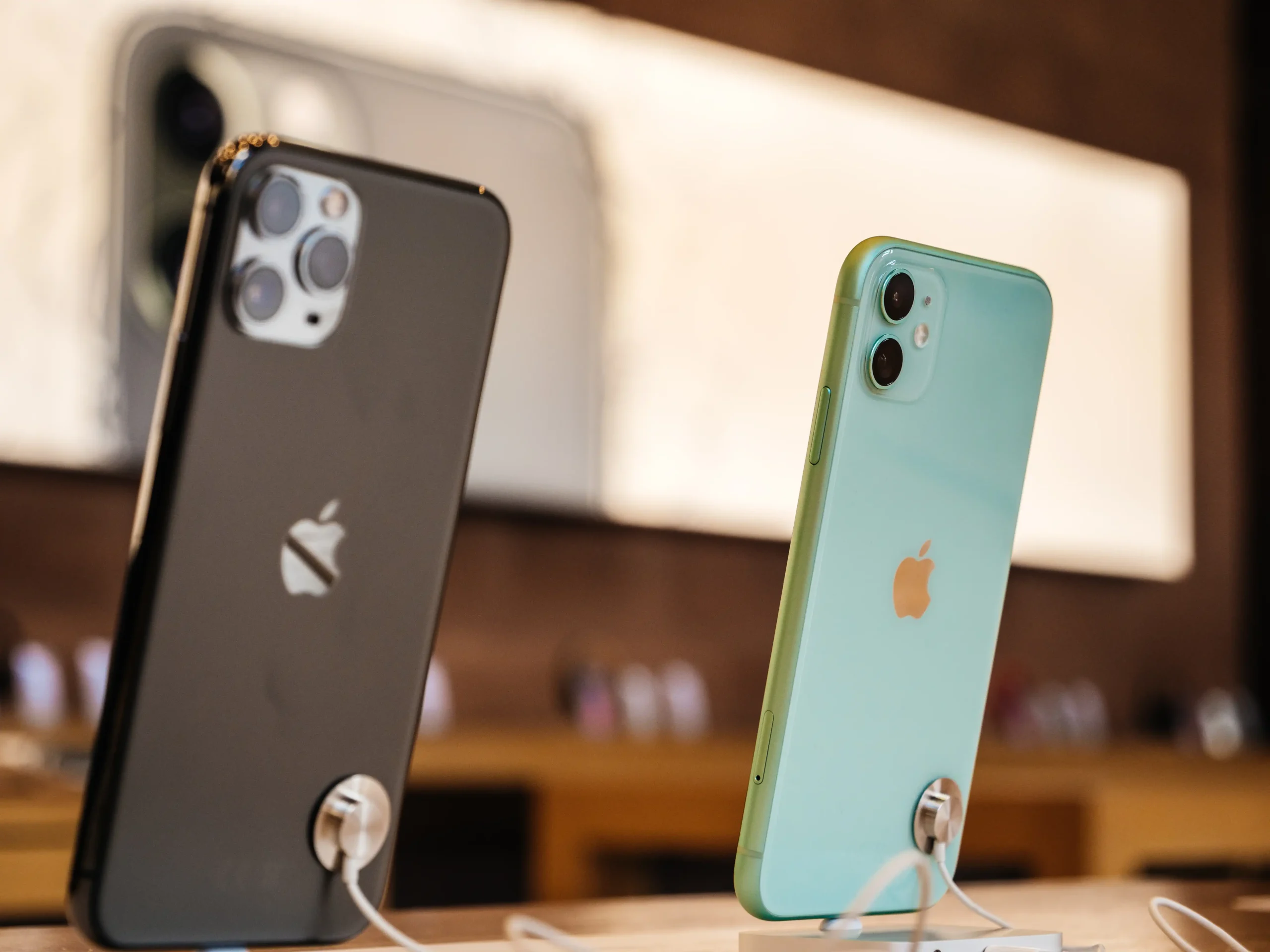 Dois celulares iPhones, nas cores preto e verde, expostos em expositor