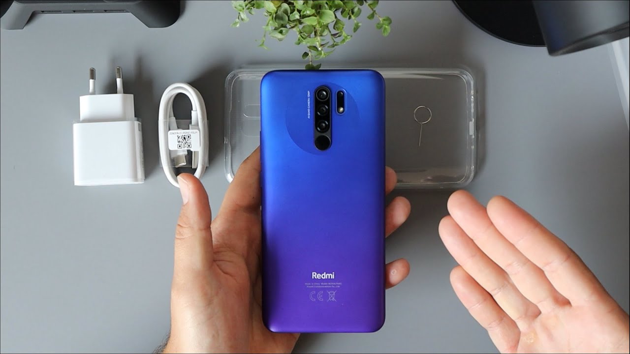 Pessoa mostrando um celular Xiaomi Redmi 9 na cor azul, com carregador branco ao lado