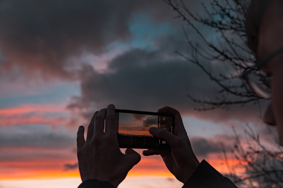 Uma pessoa está tirando foto do nascer do sol com o seu celular na mão