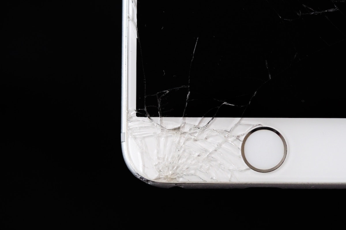 Imagem de um celular branco com tela quebrada