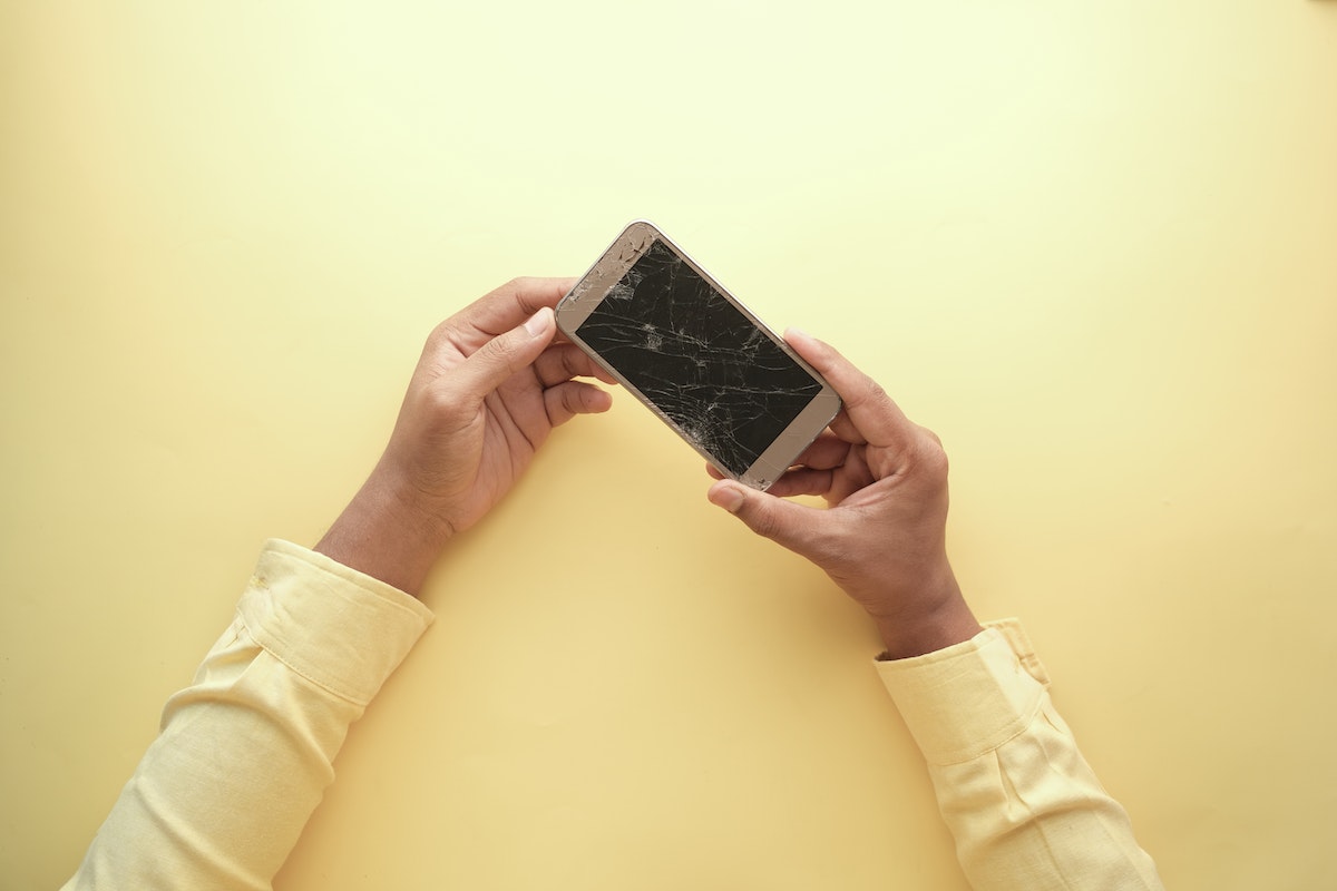 um homem segurando um celular com a tela quebrada após ver que não tem uma película de celular que não quebra