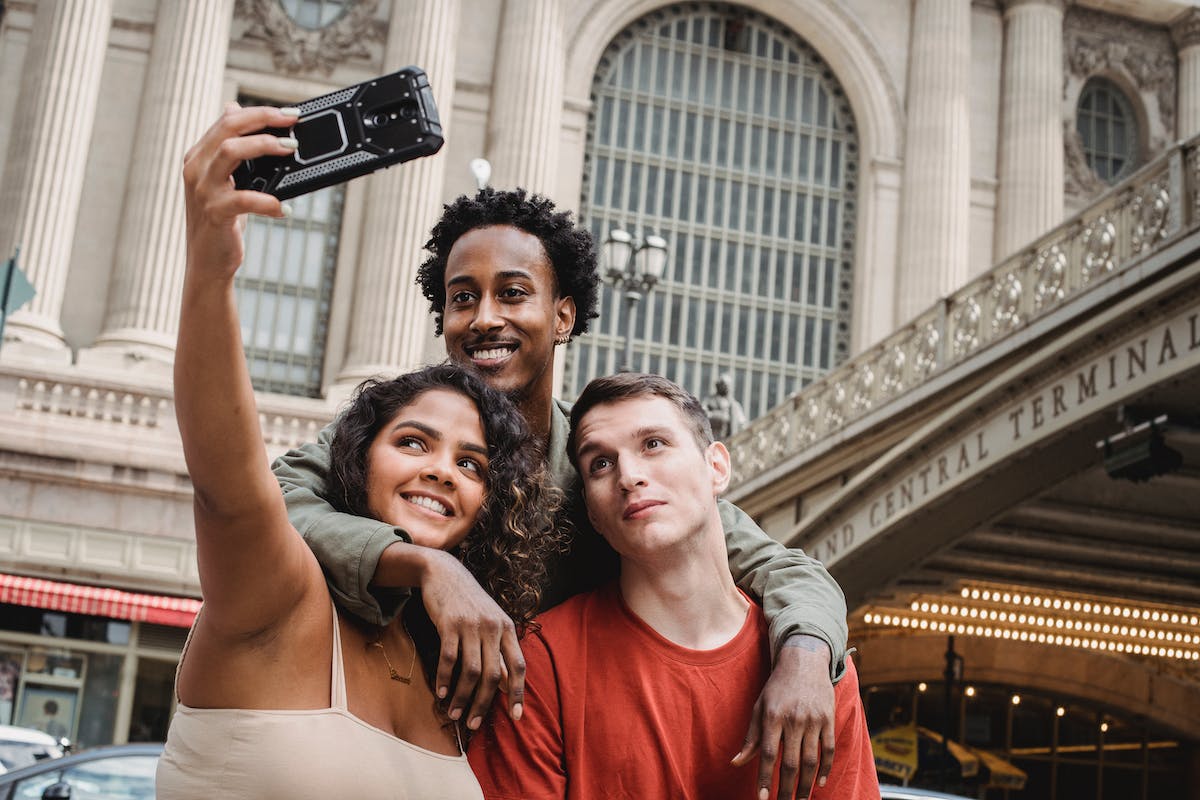 Três amigos estão em frente a um prédio tirando uma selfie