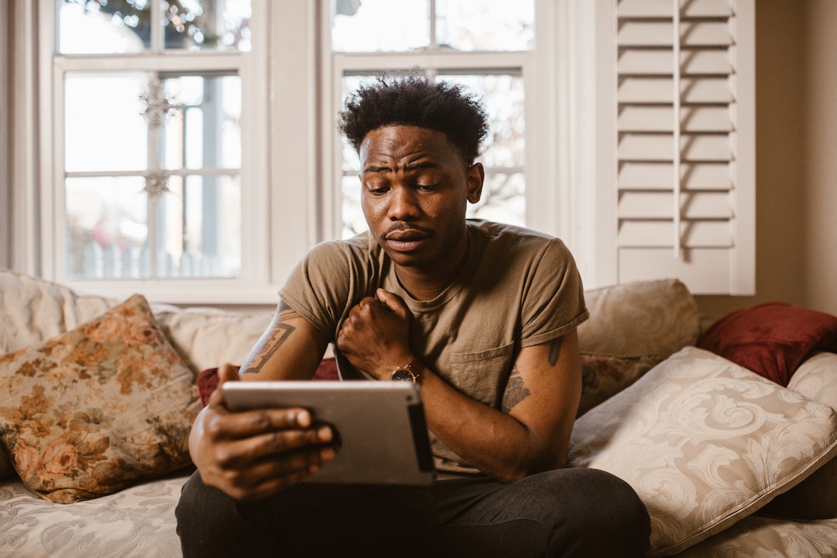 Um homem com o tablet na mão, sentado no sofá, procurando o que assistir