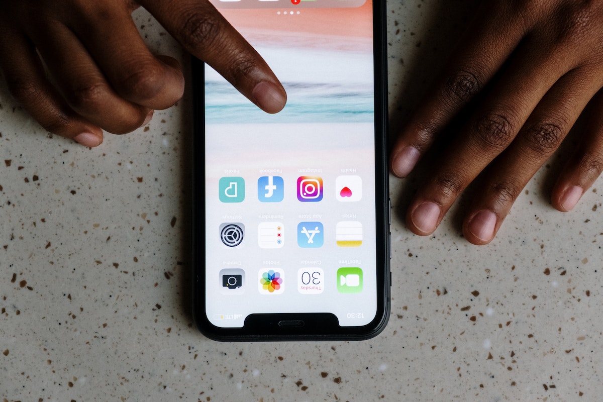 Uma pessoa está com o smartphone na mesa enquanto escolhe um aplicativo na tela inicial