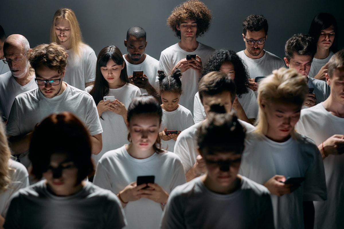 um grupo de pessoas estão uma ao lado da outra com a cabeça baixa olhando para o smartphone, pesquisando como comprar um celular novo