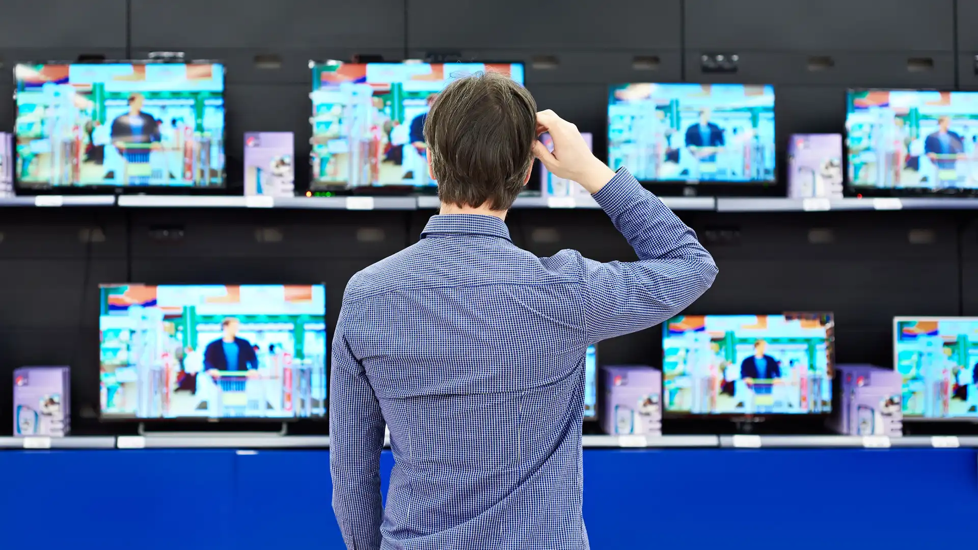 Homem parado olhando vários televisores em uma loja