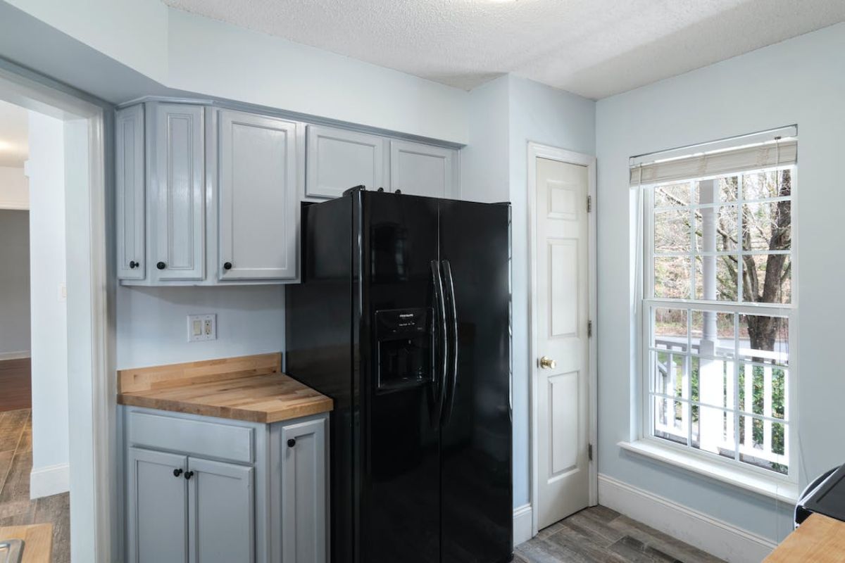 Uma cozinha totalmente branca onde há uma geladeira preta de duas portas