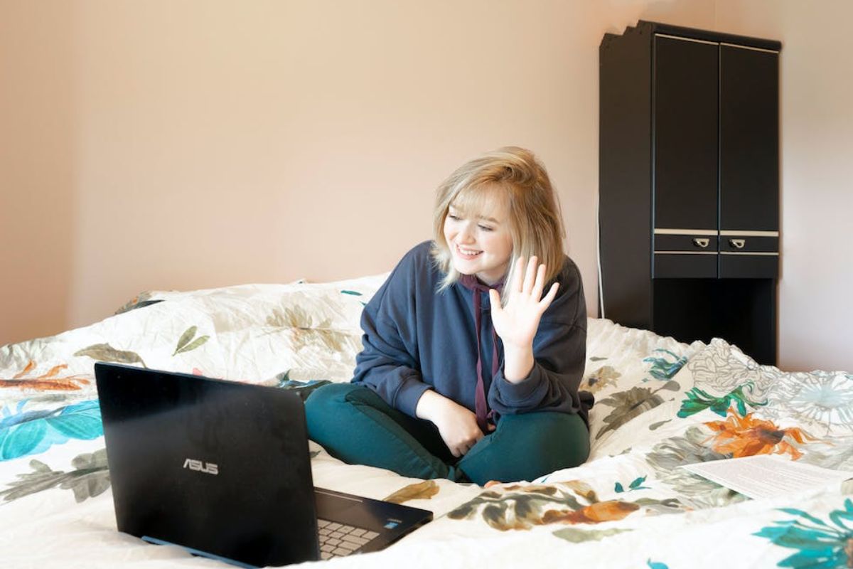 Uma mulher está sentada na cama e acena para a câmera do seu notebook Asus