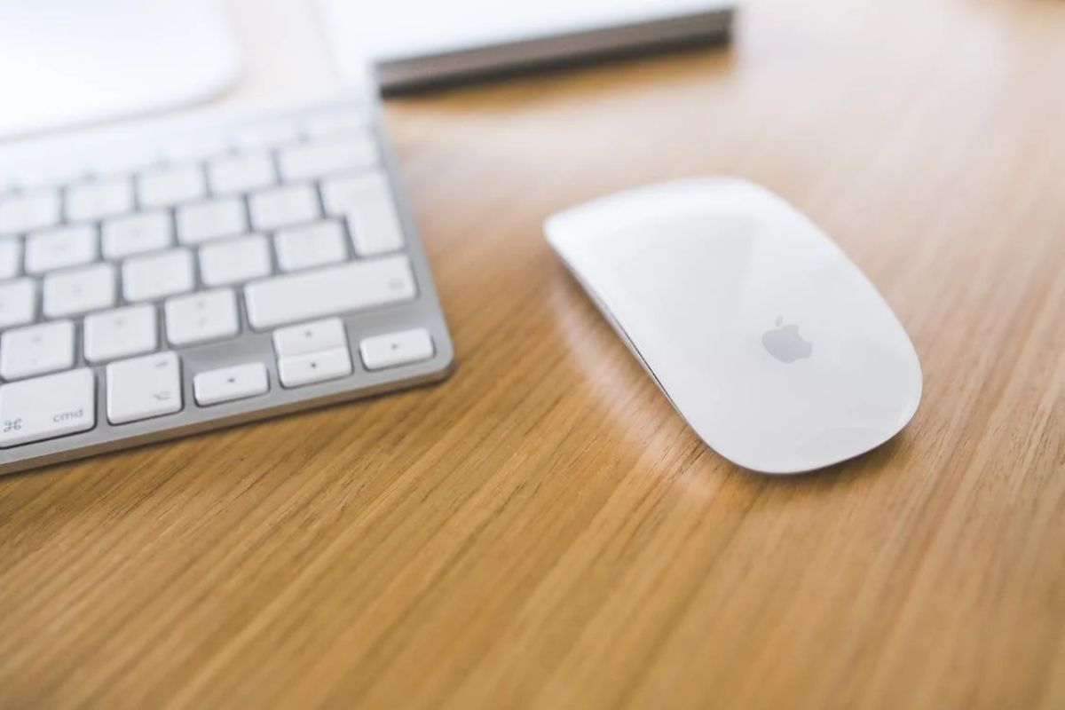 Um magic mouse está ao lado de um teclado em cima de uma superfície de madeira