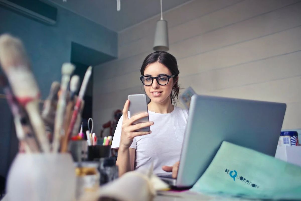 Uma menina segura um celular enquanto está na frente de um Notebook Asus, Acer ou Lenovo