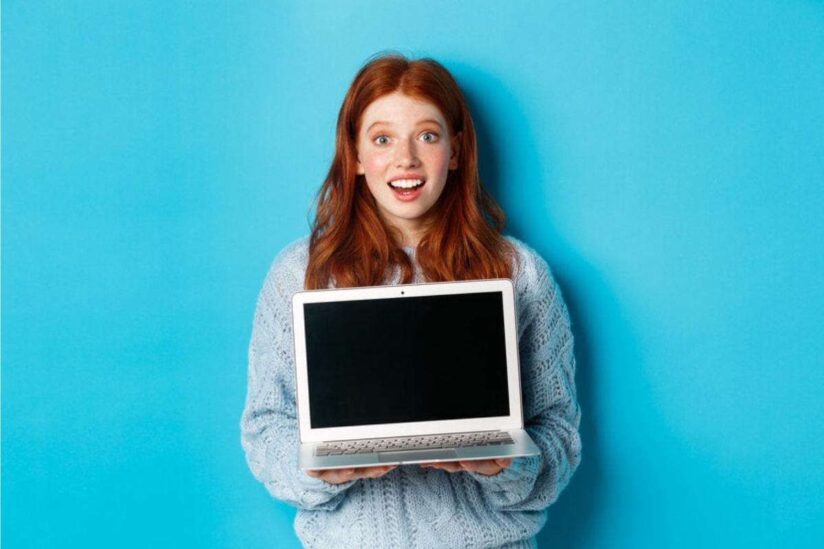 Uma mulher está segurando um notebook com tela preta, ao fundo há a cor azul