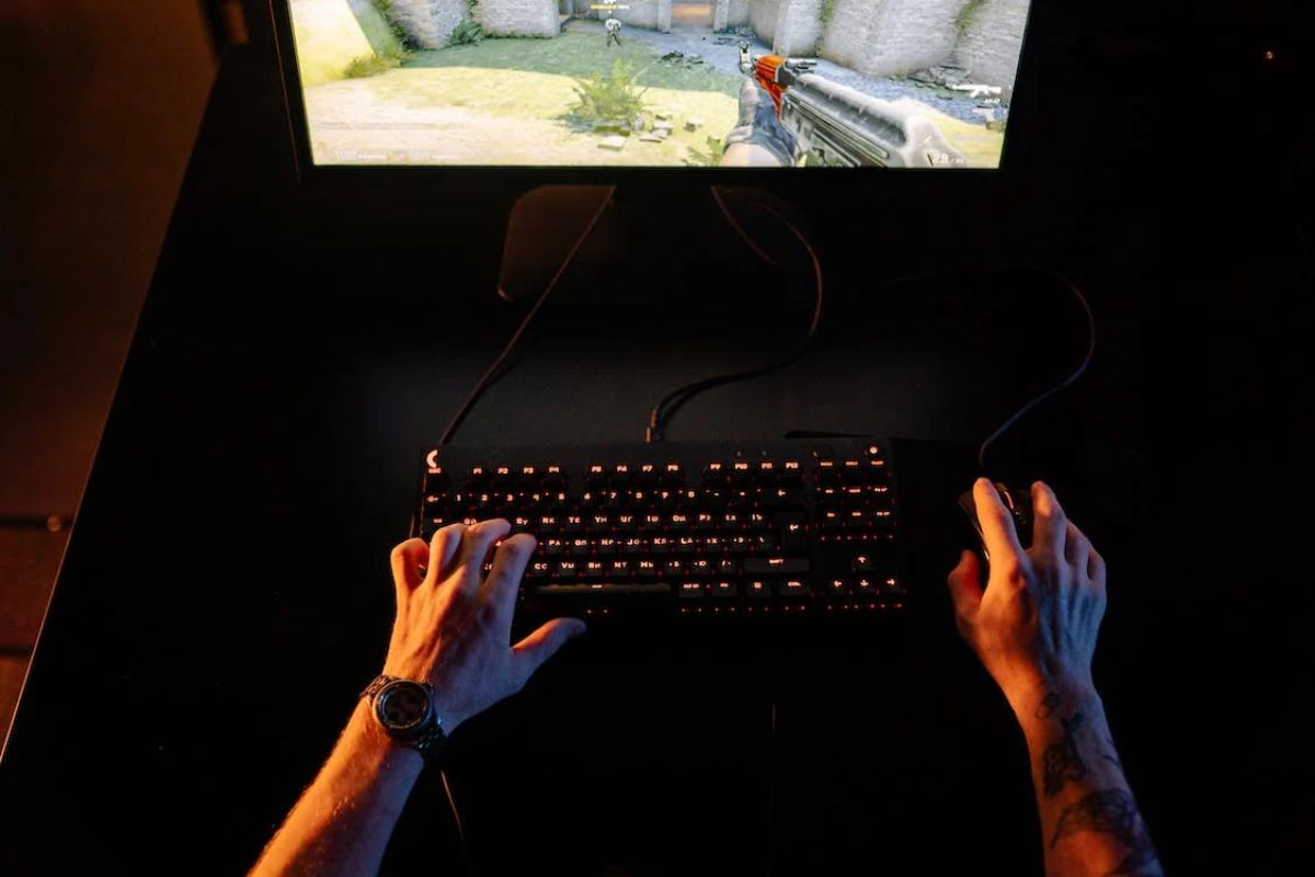 As mãos de uma pessoa jogando FPS com um teclado retroiluminado em uma Mesa para Computador Gamer