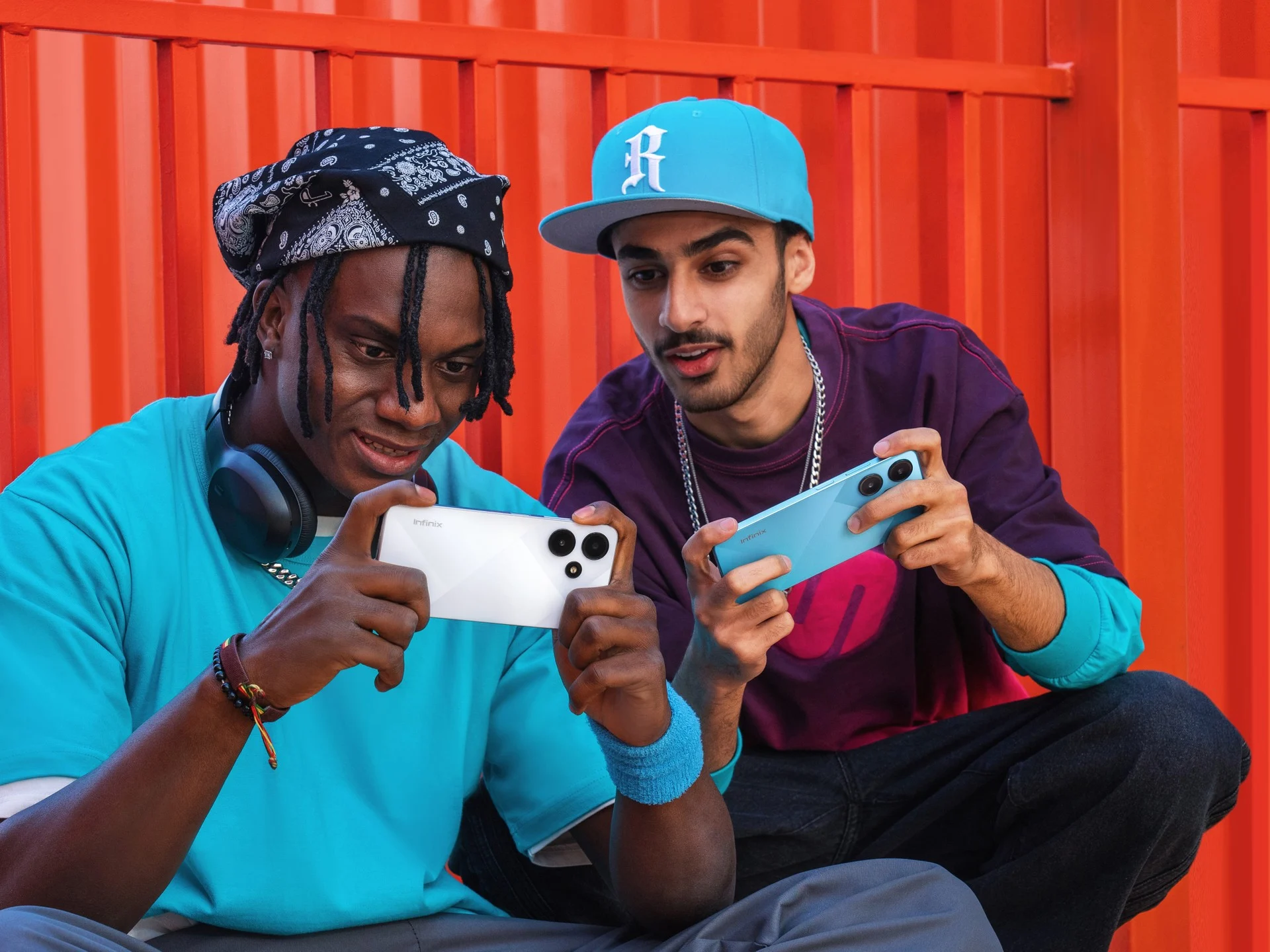 Da esquerda para direita: homem usando camiseta azul, e segurando um celular branco. Homem de bone azul e camiseta preta, segurando um celular azul