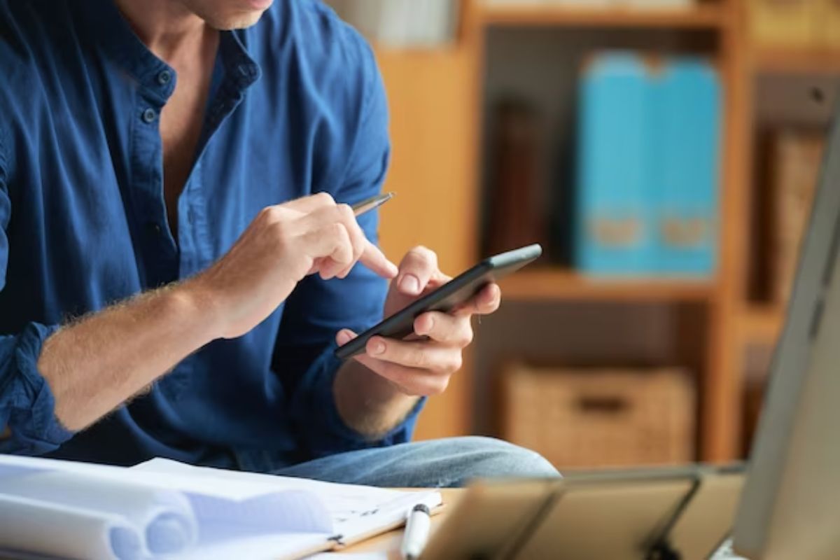 Um homem está com o celular na mão. Aparece apenas uma parte de seu busto enquanto ele toca no aplicativo