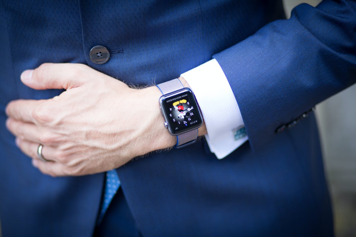 Um homem vestindo um terno e um relógio de pulso Apple Watch Series 4 está olhando para um smartphone iPhone 14 Pro Max em sua mão, que é um smartwatch conta frequências cardíacas