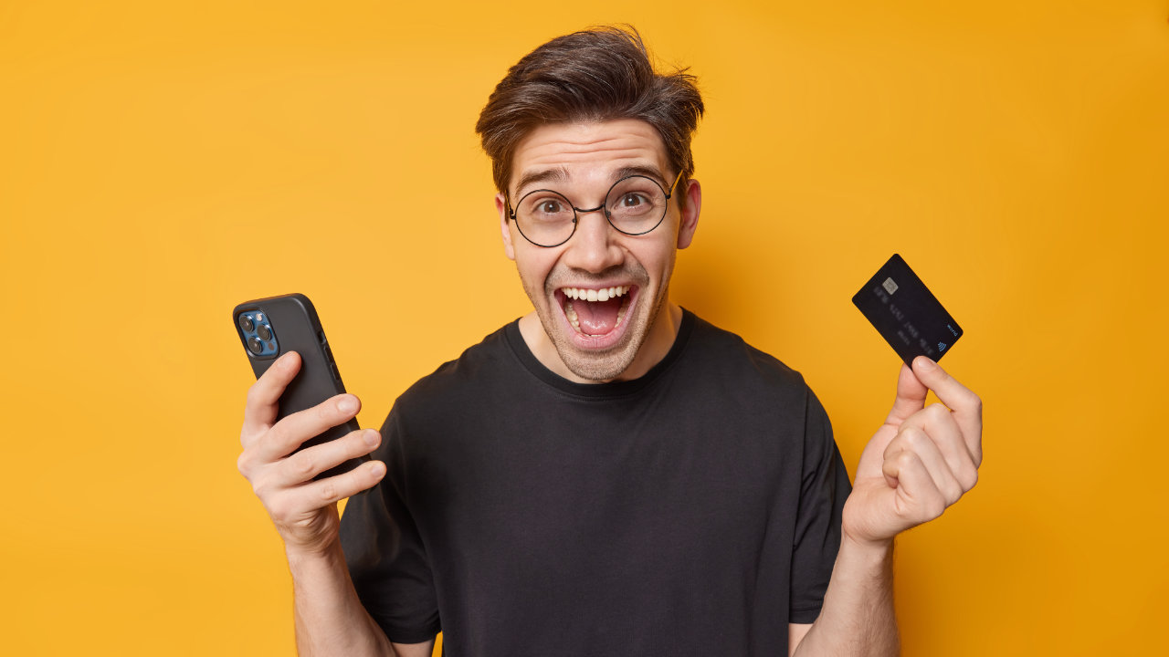 Homem eufórico com celular em uma mão e cartão de crédito na outra