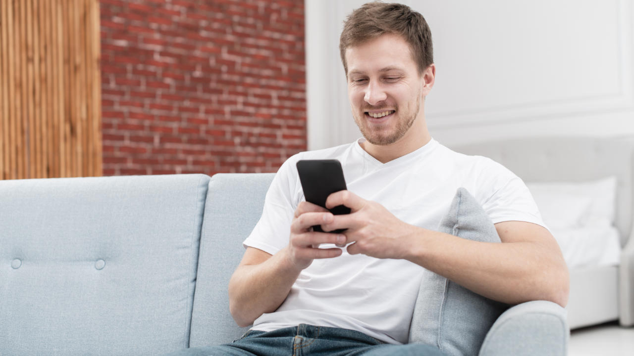 Homem sentado no sofá com celular na mão