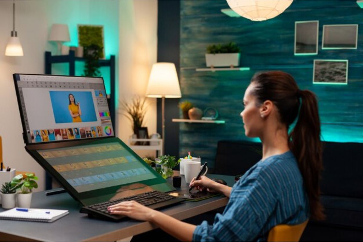 Uma mulher está sentada em frente ao seu computador e tem uma mesa digital onde edita os seus vídeos