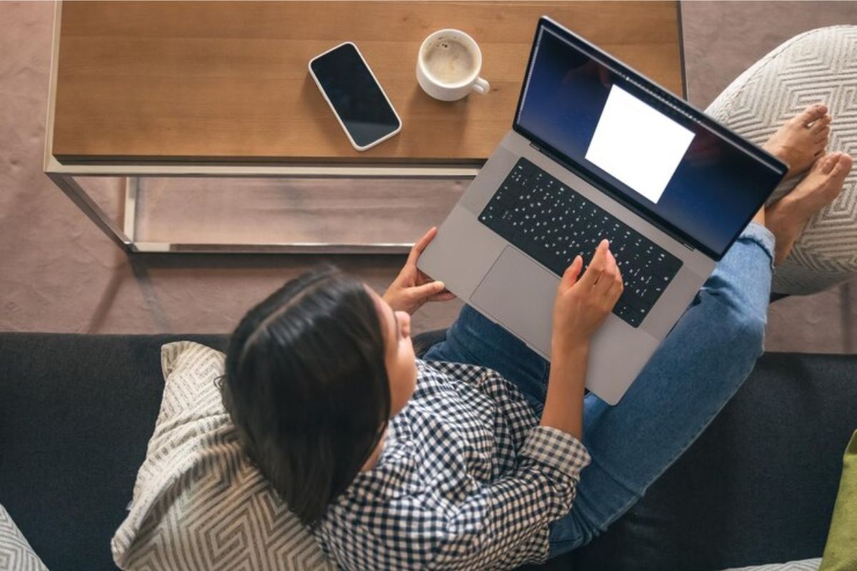 Uma mulher sentada com o notebook no colo enquanto