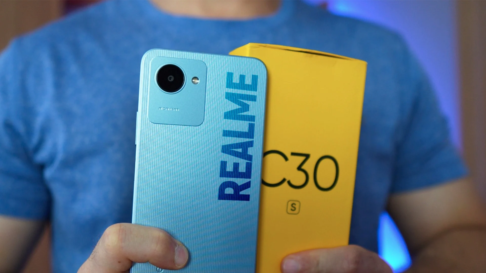 homem segurando um celular realme C30 azul, ao lado da embalagem