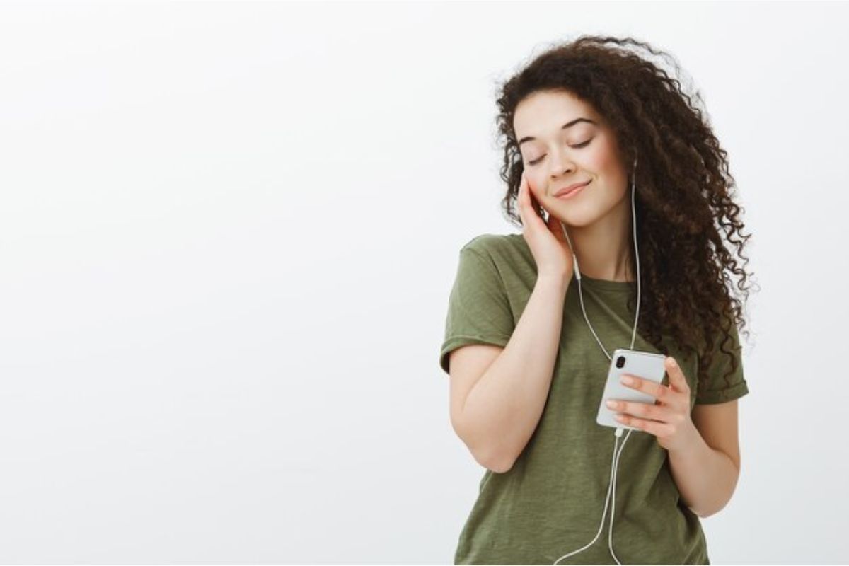 Uma mulher está com um celular na mão, e no fone de ouvindo escuta a Retrospectiva no Spotify 2023