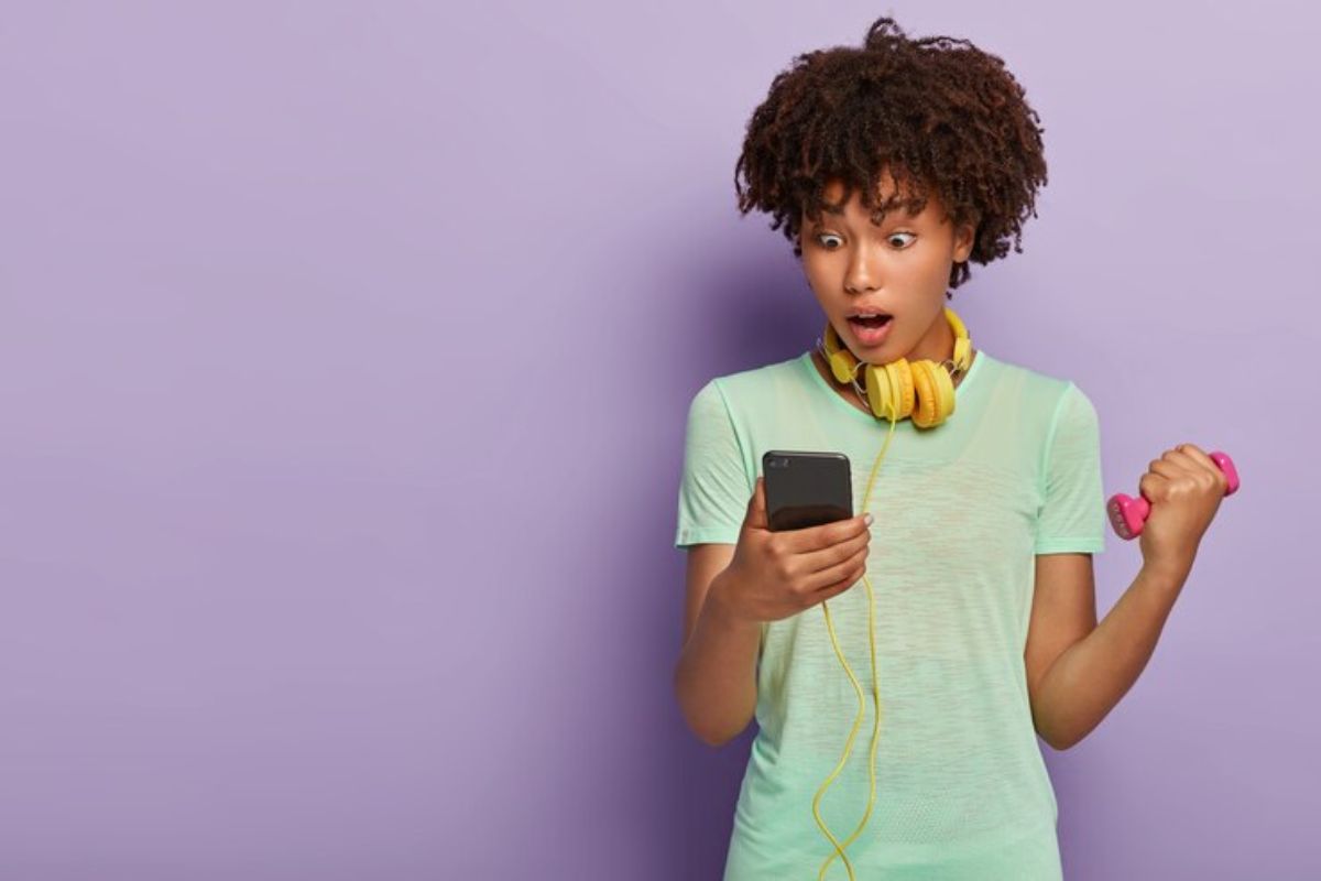 Uma menina segura um celular na mão enquanto olha pra ele e procura Como ver a Retrospectiva no Spotify 2023