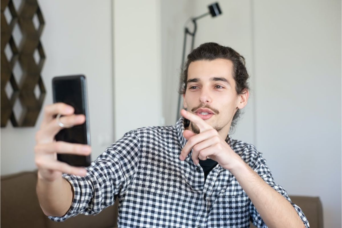 Um homem segura um celular na mão enquanto faz pose para sua selfie