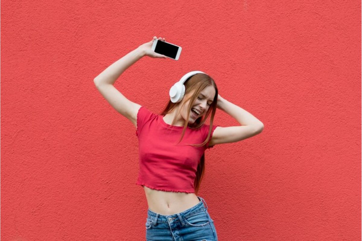 Uma menina dançando com o headphone, segurando o celular na mão enquanto dança