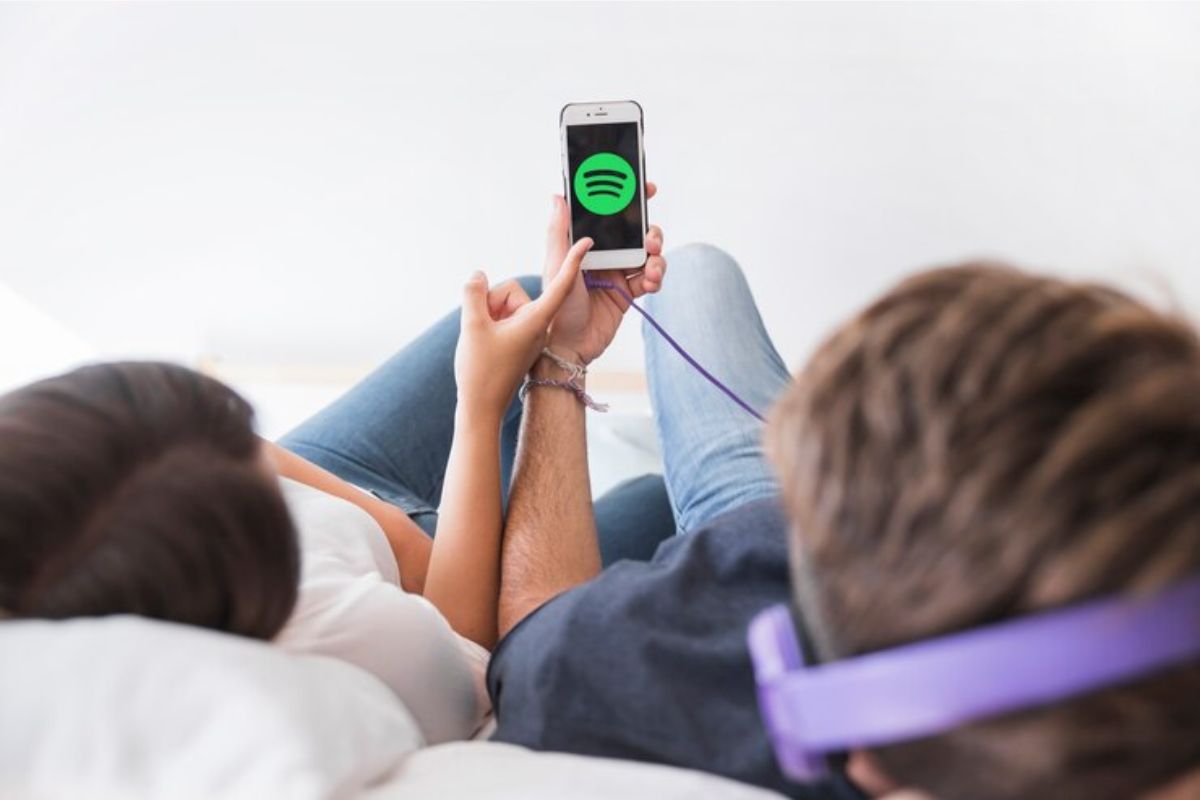 Um casal está deitado na cama enquanto na tela aparece o símbolo do Spotify