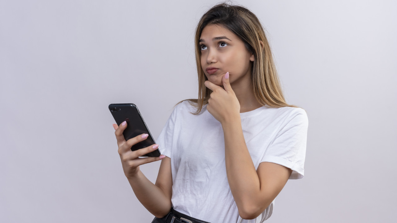 Garota com celular na mão em dúvida de quanto gastar no melhoor celular custo-benefício do ano