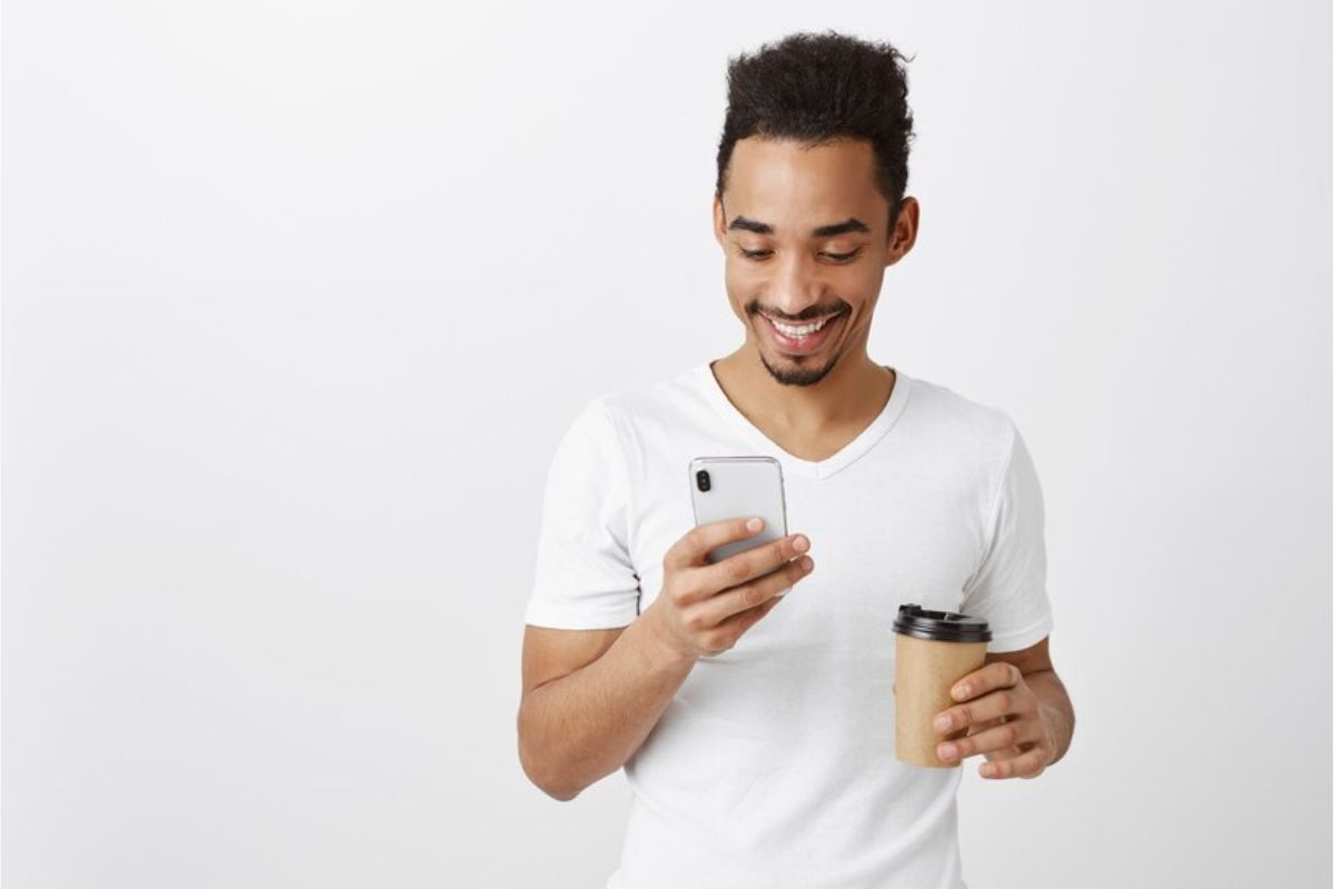 Um homem segura um celular na mão e no outro um copo de café