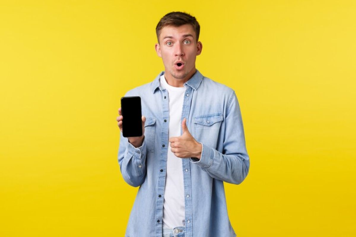 Um homem segura um celular na mão e aponta com a outra mão para ele como o melhor Celular Custo Benefício