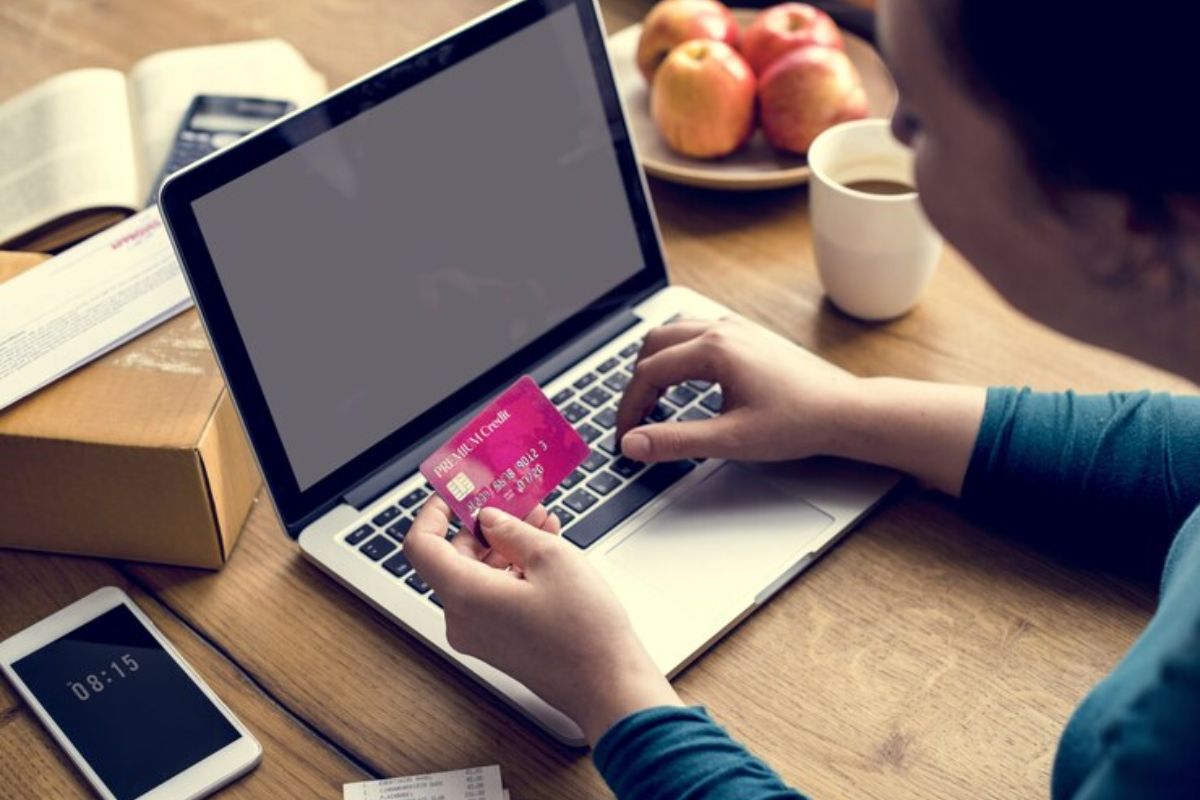 Uma mulher segura um cartão em frente ao seu notebook enquanto faz compras em Lojas Online de Eletrônicos 2024