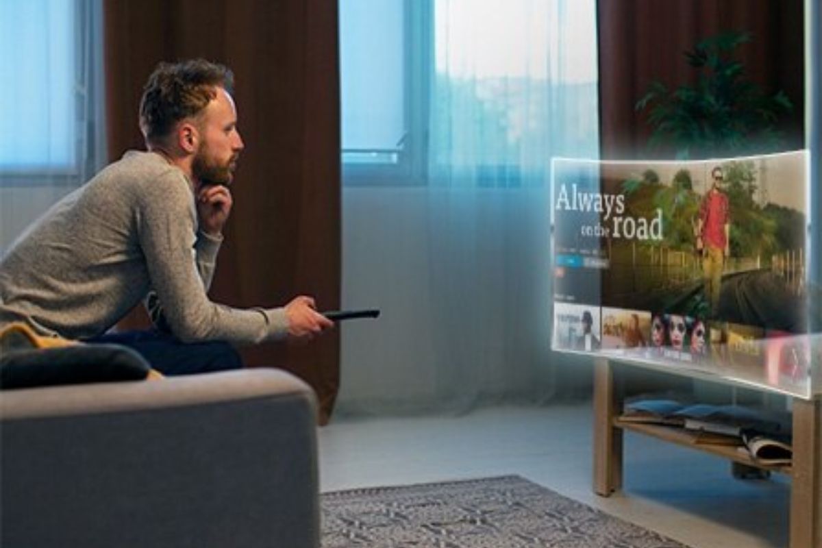 Uma pessoa sentada no sofá aponta o controle para a TV enquanto busca os Melhores Aplicativos para Smart TV de 2024