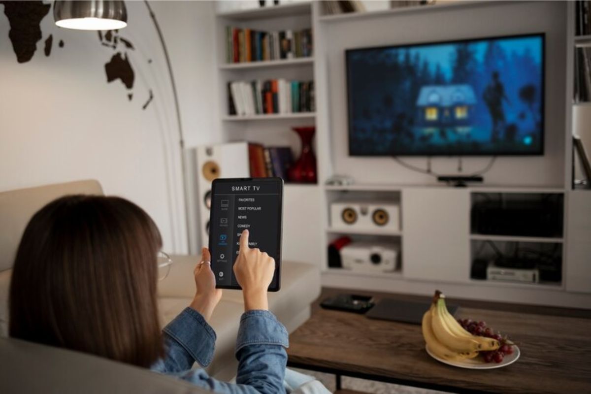 Uma menina está sentada em seu sofá. ela controla a smart tv através do tablet