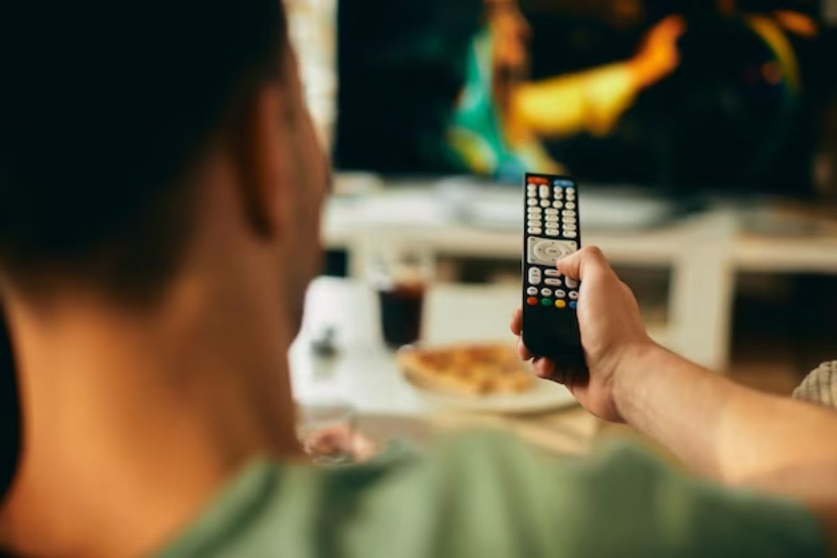 Uma pessoa sentada enquanto aponta o controle para a televisão