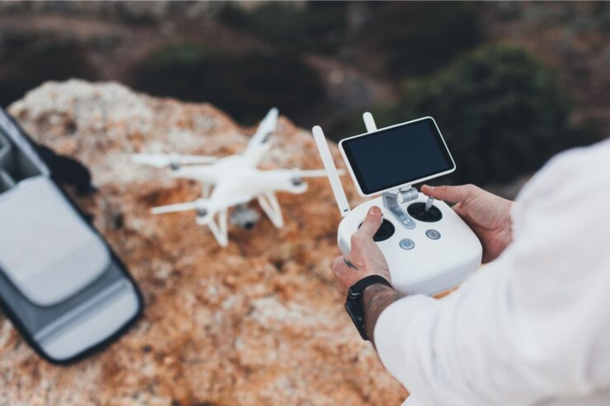 Um homem com o controle na mão. Em sua frente está o drone pousado em uma rocha