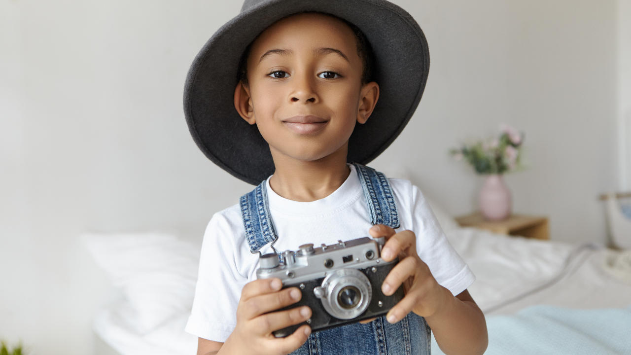Menino negro segurando câmera fotográfica infantil enquanto posa para foto